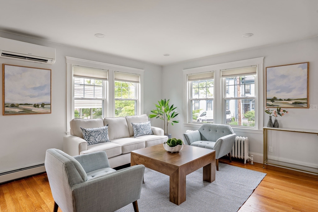 Bright living room with pale seating, a wooden coffee table, and windows on two walls.