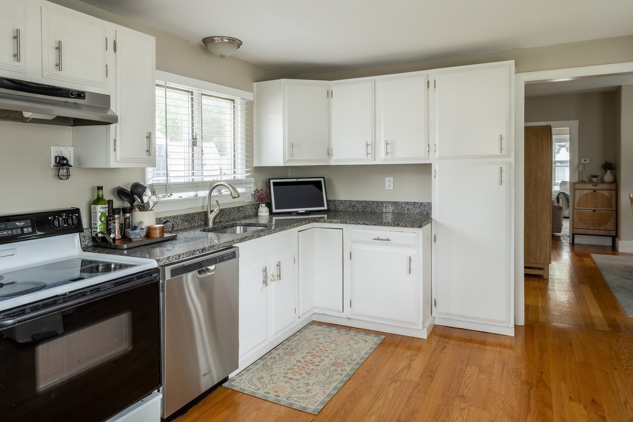 Kitchen with white cabinets, gray stone counters, a window over the sink, and hardwood floors.