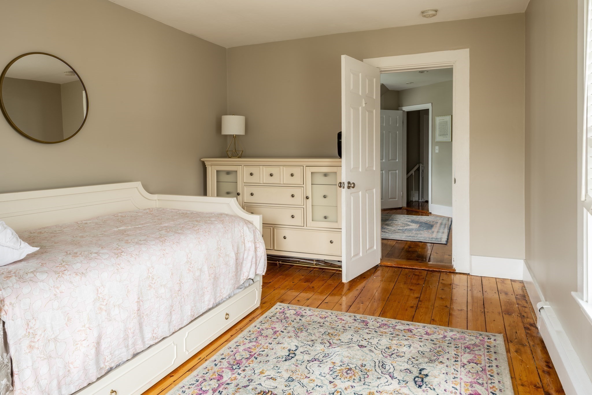 Bedroom with a white floral-quilted bed, cream dresser, and warm hardwood floors.