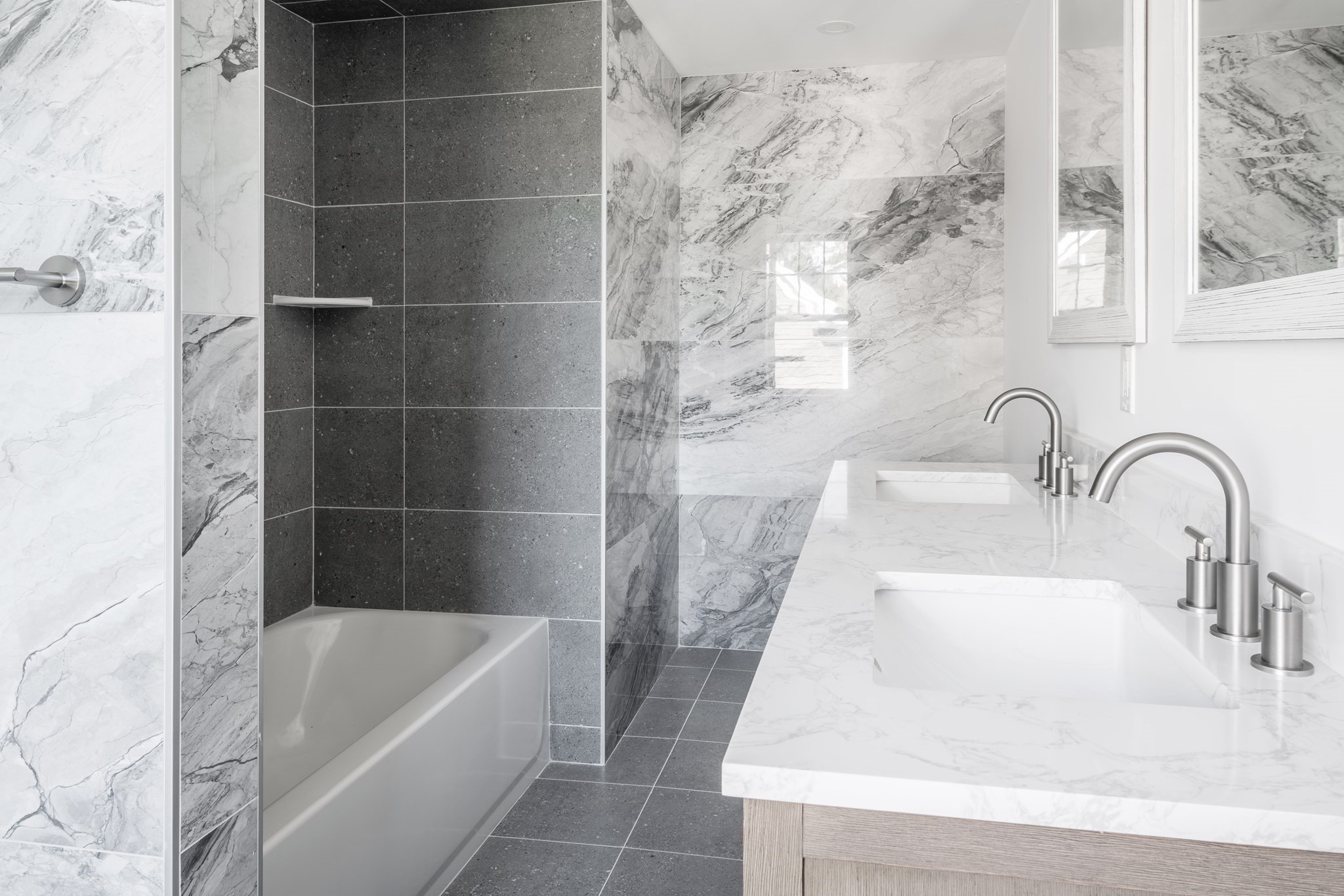 Modern bathroom with a bathtub, marble-look tile, and a white double-sink vanity.