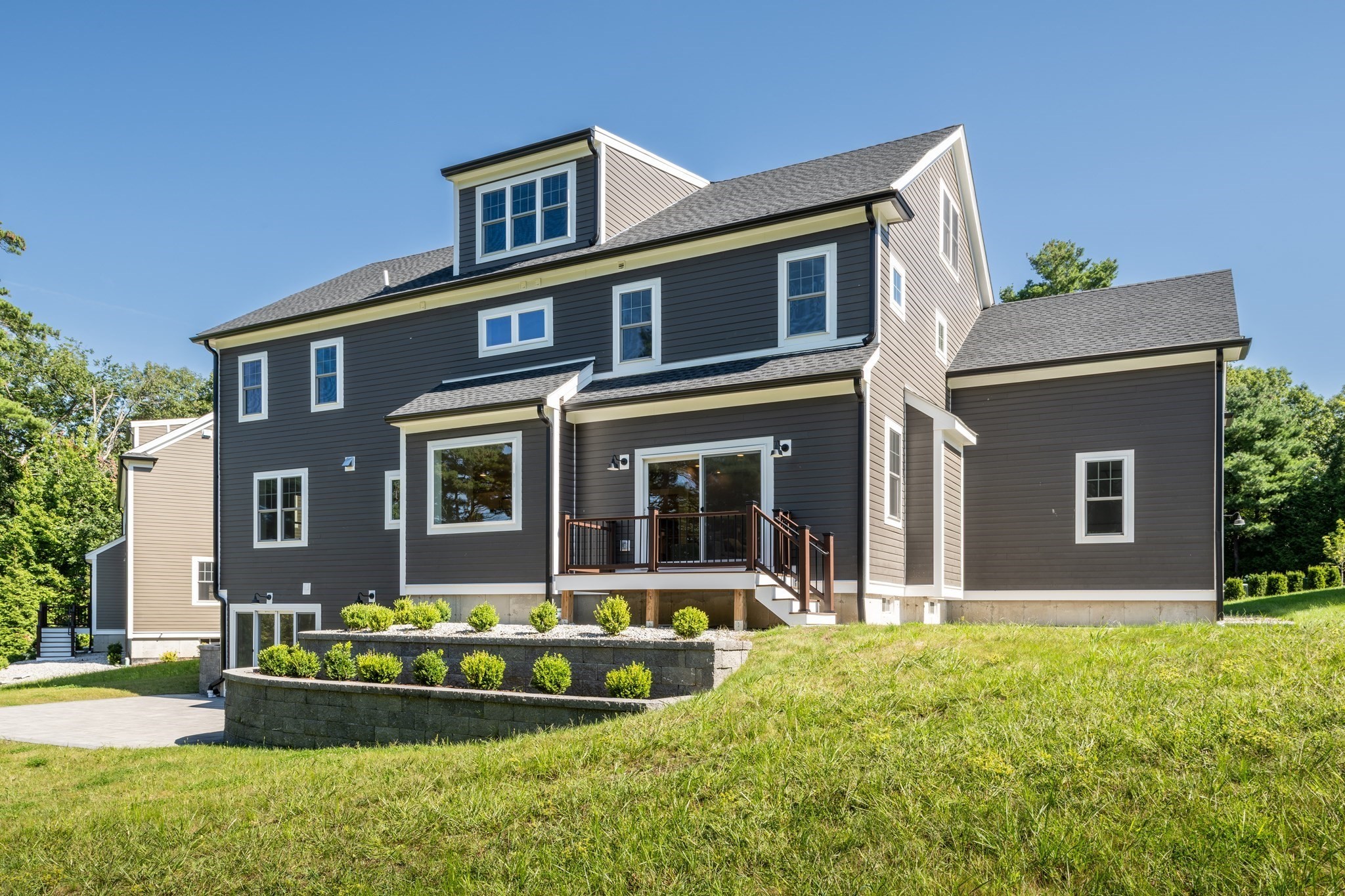Large dark gray house with white trim, raised deck, and landscaped retaining walls on a sunny day.