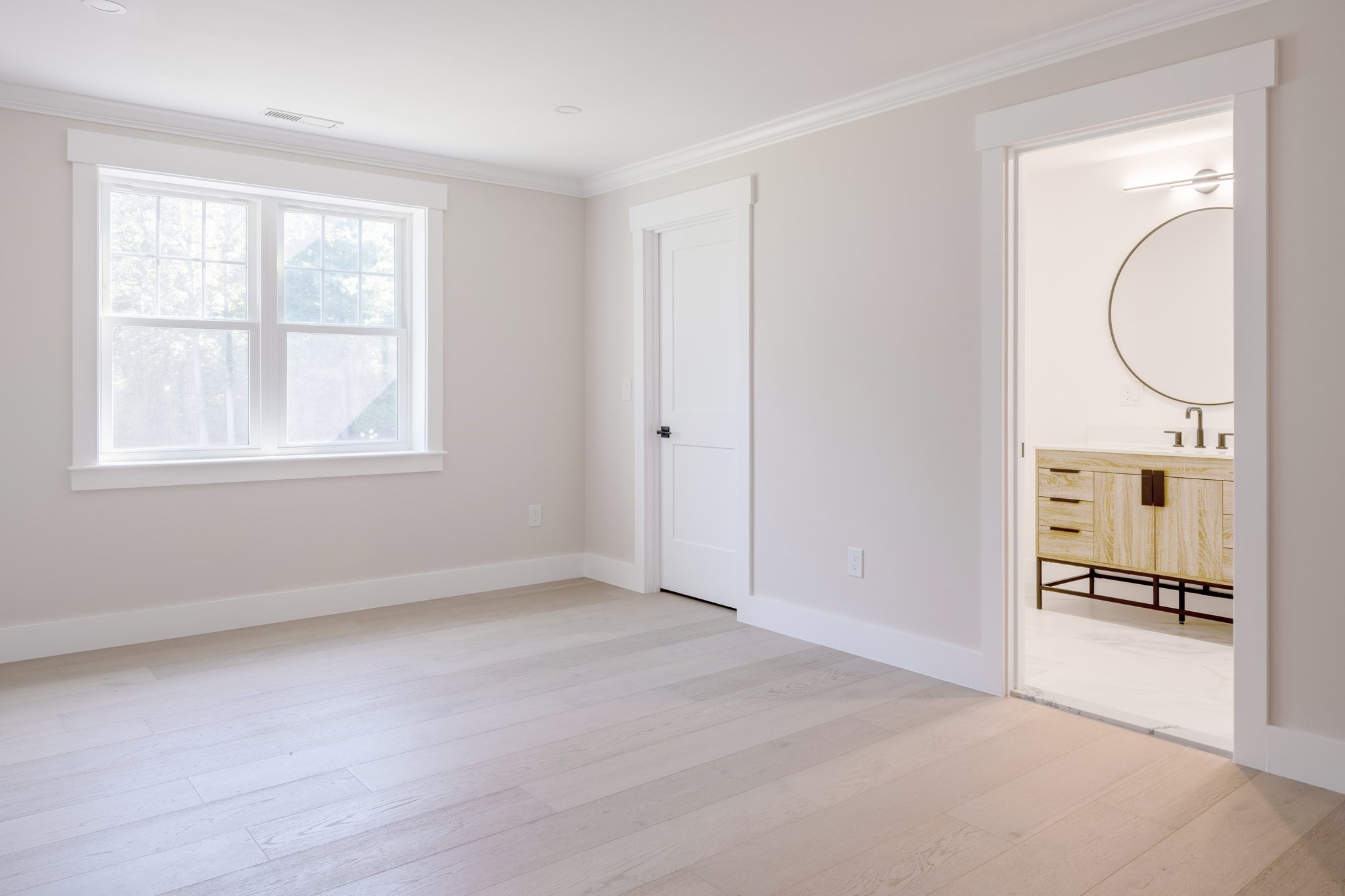 Empty bedroom with a large double window and an open doorway to an ensuite bathroom.