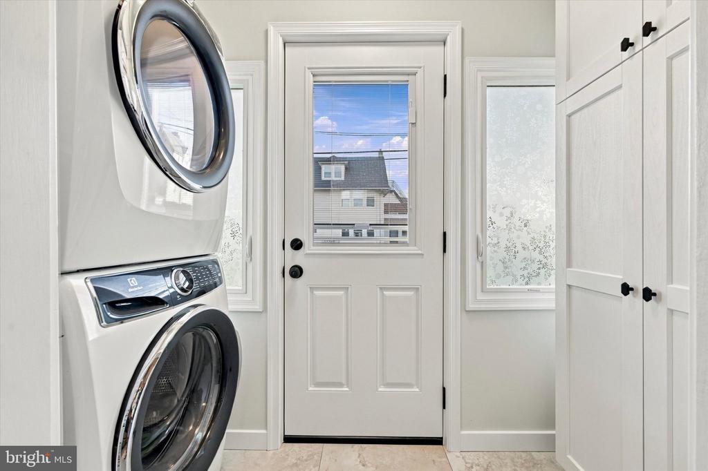 Laundry room with stacked washer and dryer, white storage cabinets, and a windowed exterior door.