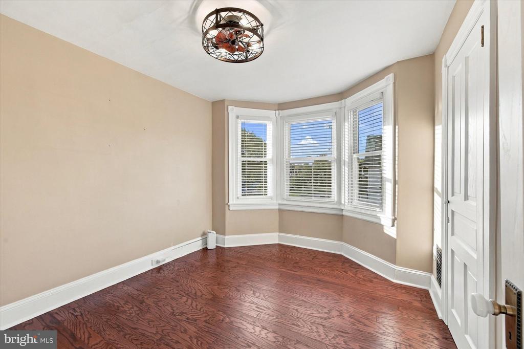 Empty room with reddish hardwood floors, a bay window, and a ceiling fan.