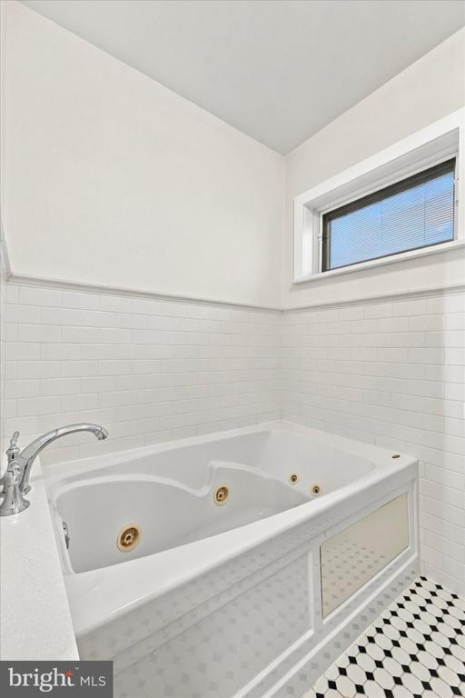 Bathroom with a built-in jetted tub, white tile, patterned floor, and high window.