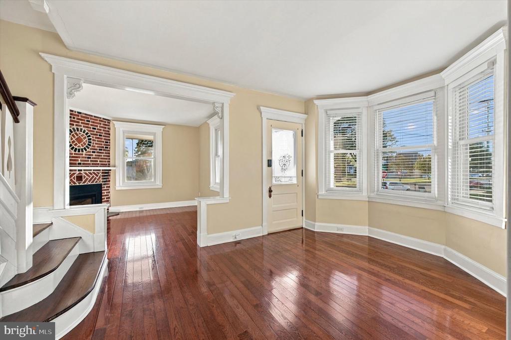 Living room with bay windows, hardwood floors, and an arched opening to a brick fireplace.