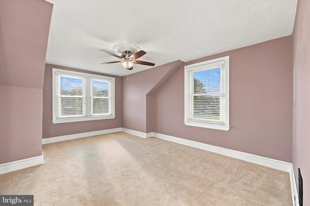 Empty bedroom with mauve walls, patterned beige carpet, and a ceiling fan.