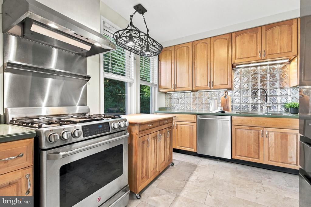 Kitchen with honey-toned cabinets, patterned tile backsplash, and a large stainless steel gas range.