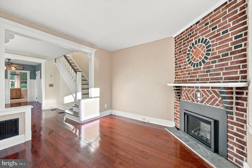 Vacant living room with hardwood floors, brick fireplace, and staircase.