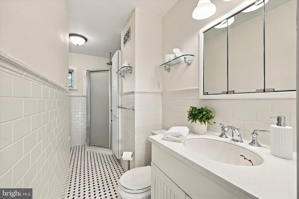 Bathroom with white subway tile, glass shower, long vanity, and black-and-white patterned floor.