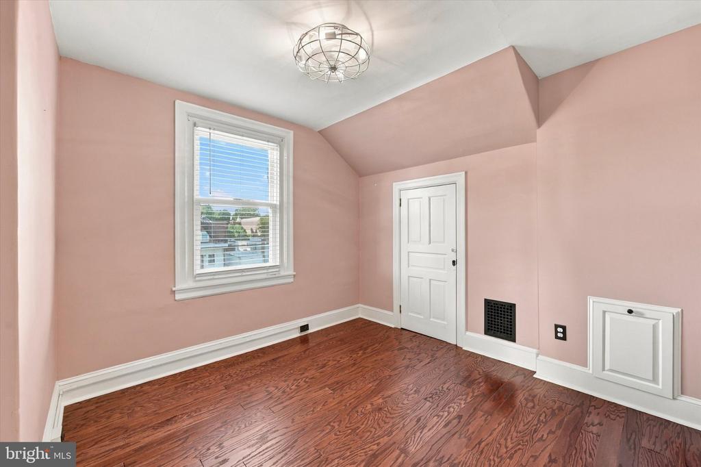Empty pink room with hardwood floors, a high angled ceiling, and a large window.