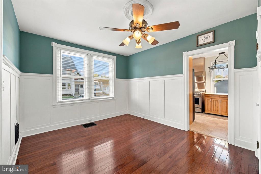 Empty room with teal walls, white wainscoting, polished hardwood floors, and a doorway to the kitchen.
