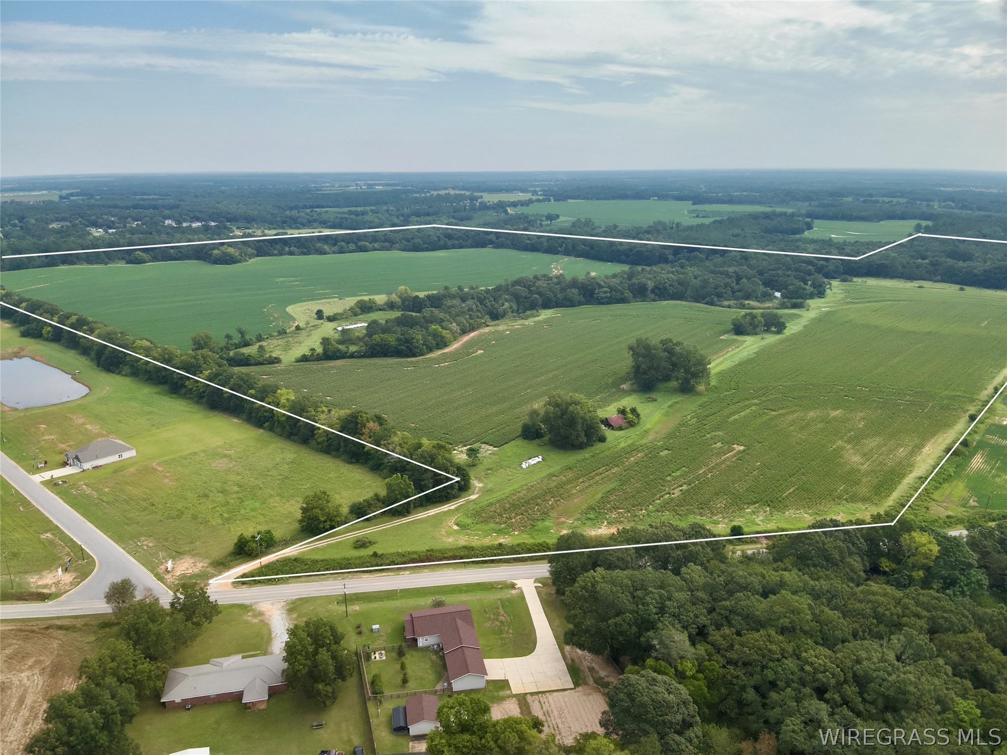 Aerial view of a large outlined rural property with cultivated fields, trees, pond, and road frontage.