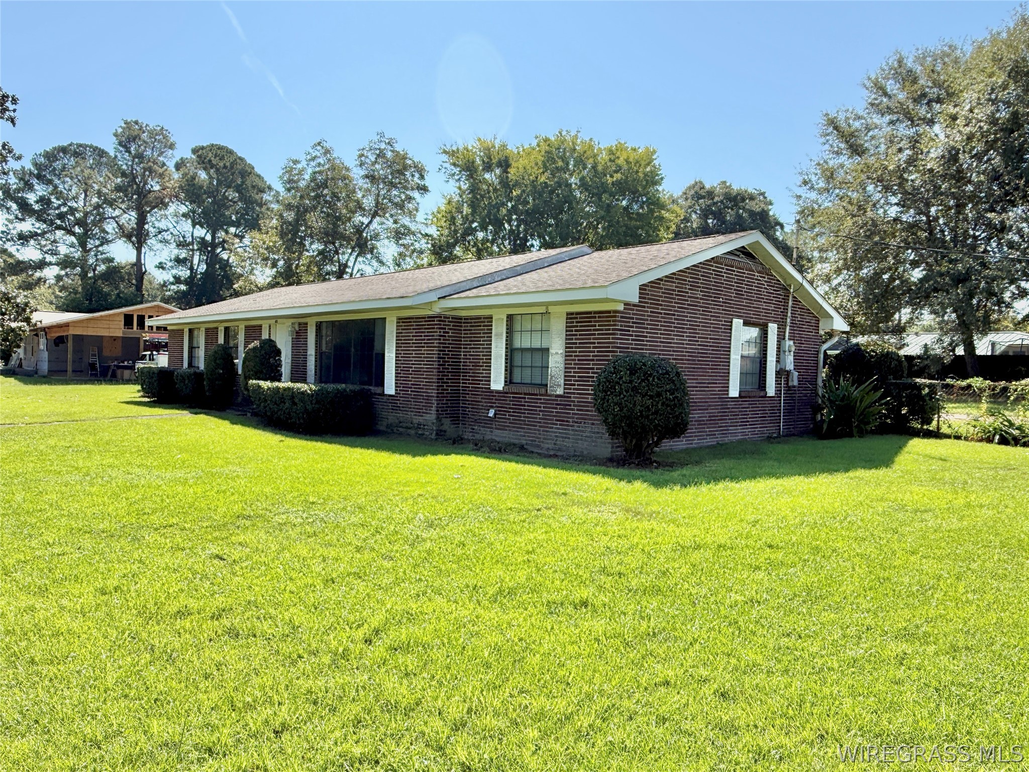 Brick ranch house with white trim, rounded shrubs, and a broad green lawn.
