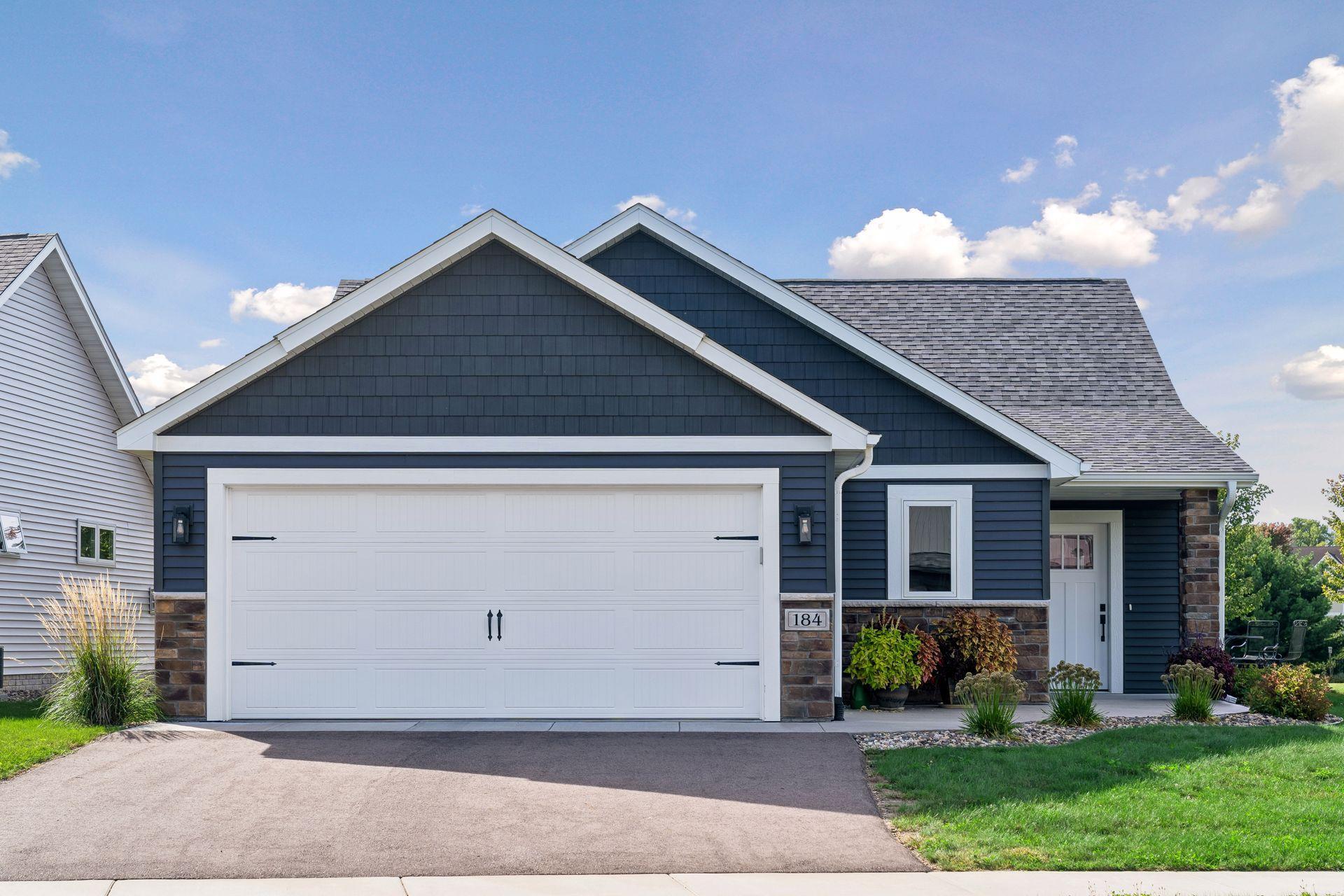 Dark blue home with white trim, a wide garage door, stone accents, and landscaped beds.