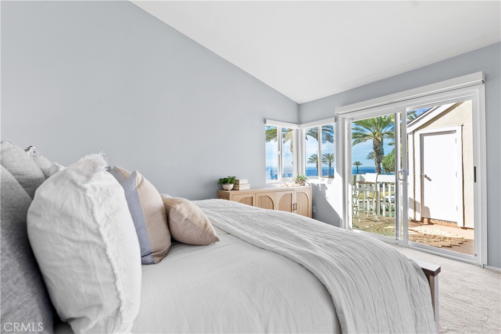 Bedroom with a white bed and sliding doors opening to a patio with palm trees and ocean views.