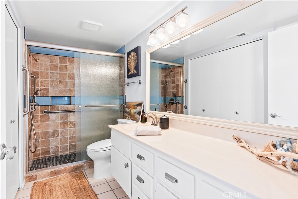 Bathroom with a long white vanity and tiled walk-in shower with frosted glass and grab bars.