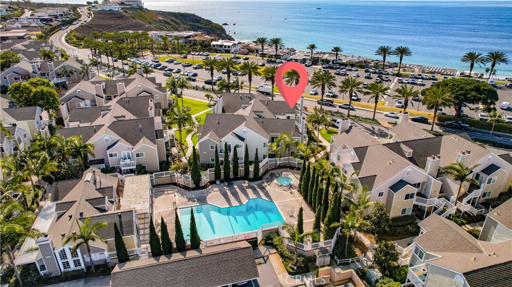 Aerial view of coastal homes, a swimming pool, and ocean, with a red marker over one residence.