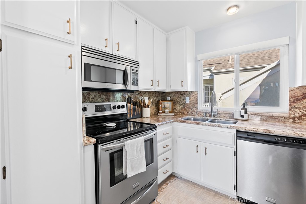 Kitchen with white cabinets, stone counters, stainless steel appliances, and a window over the sink.