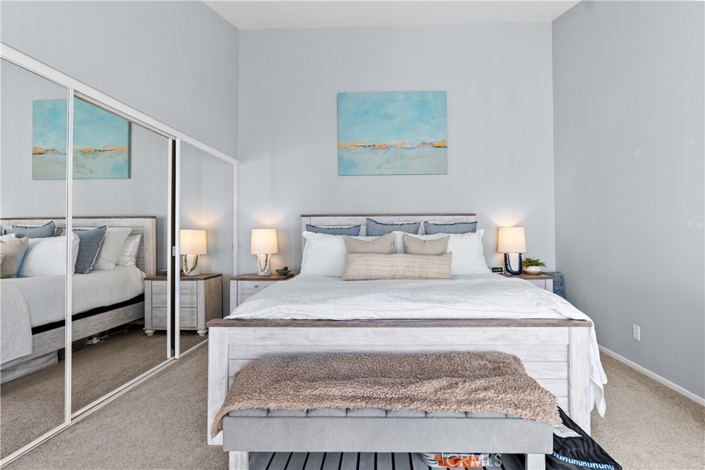 Staged bedroom with a large bed, mirrored closet doors, and blue coastal artwork.