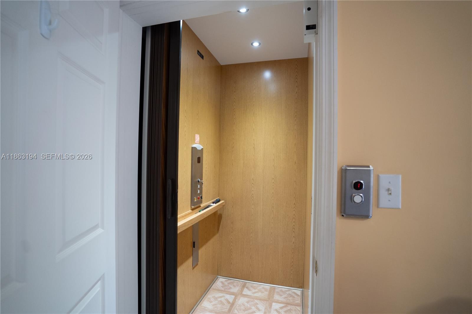 Open elevator with wood-paneled walls, a control panel, and patterned tile flooring.