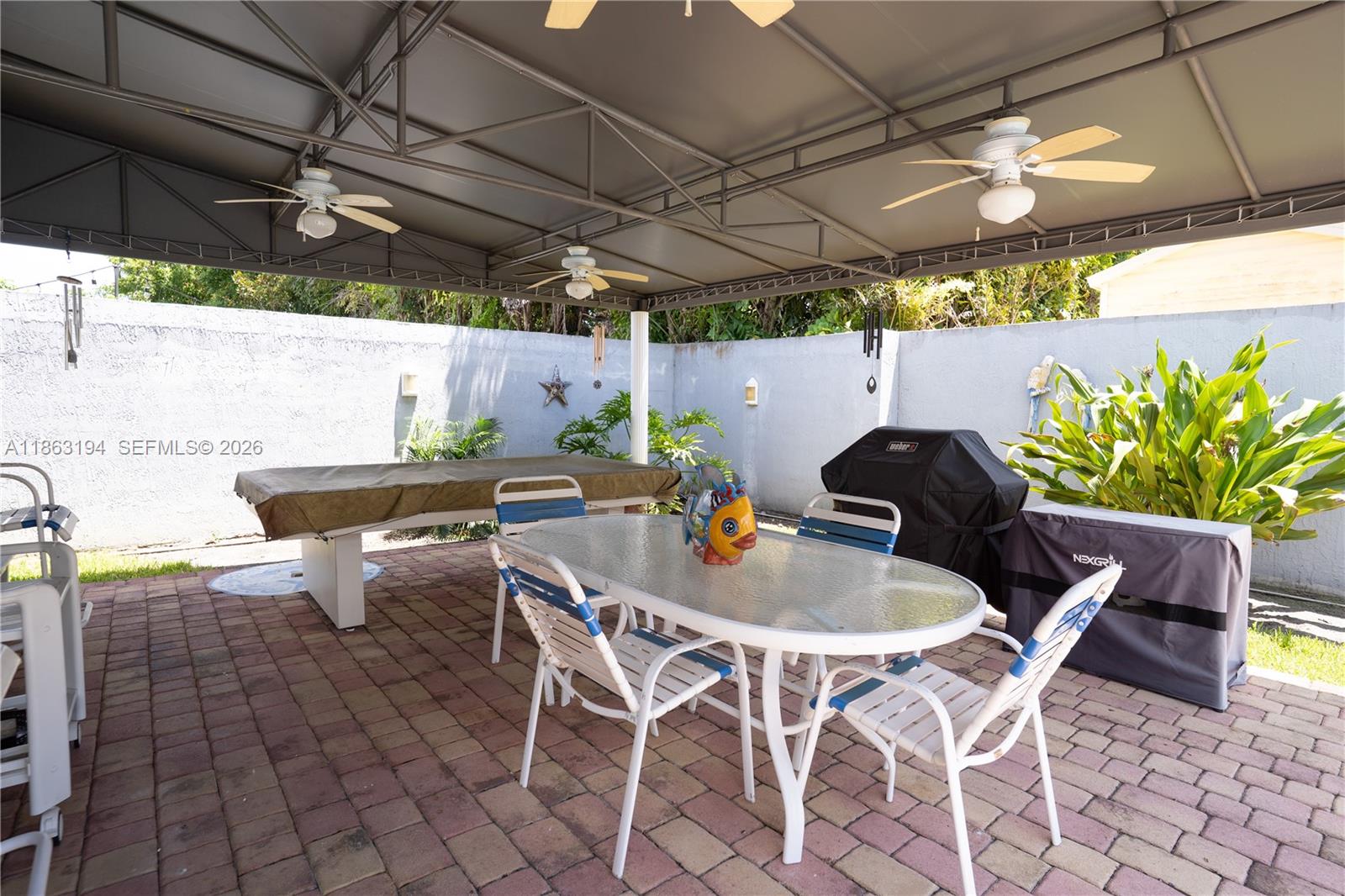 Covered patio with a glass-top dining table, brick pavers, ceiling fans, and tropical plants.