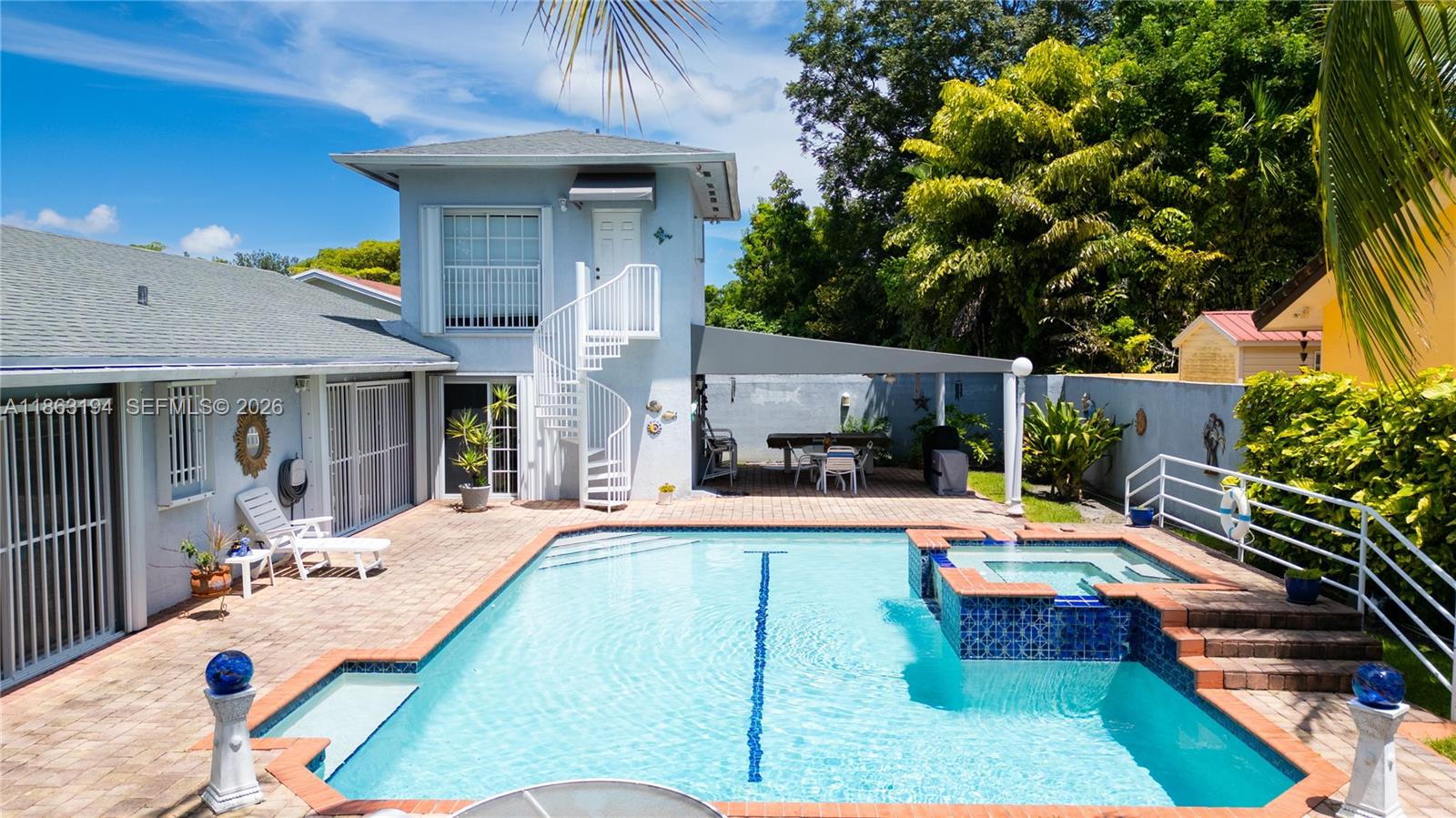 Backyard swimming pool with attached spa, brick pavers, and a white spiral staircase beside the home.