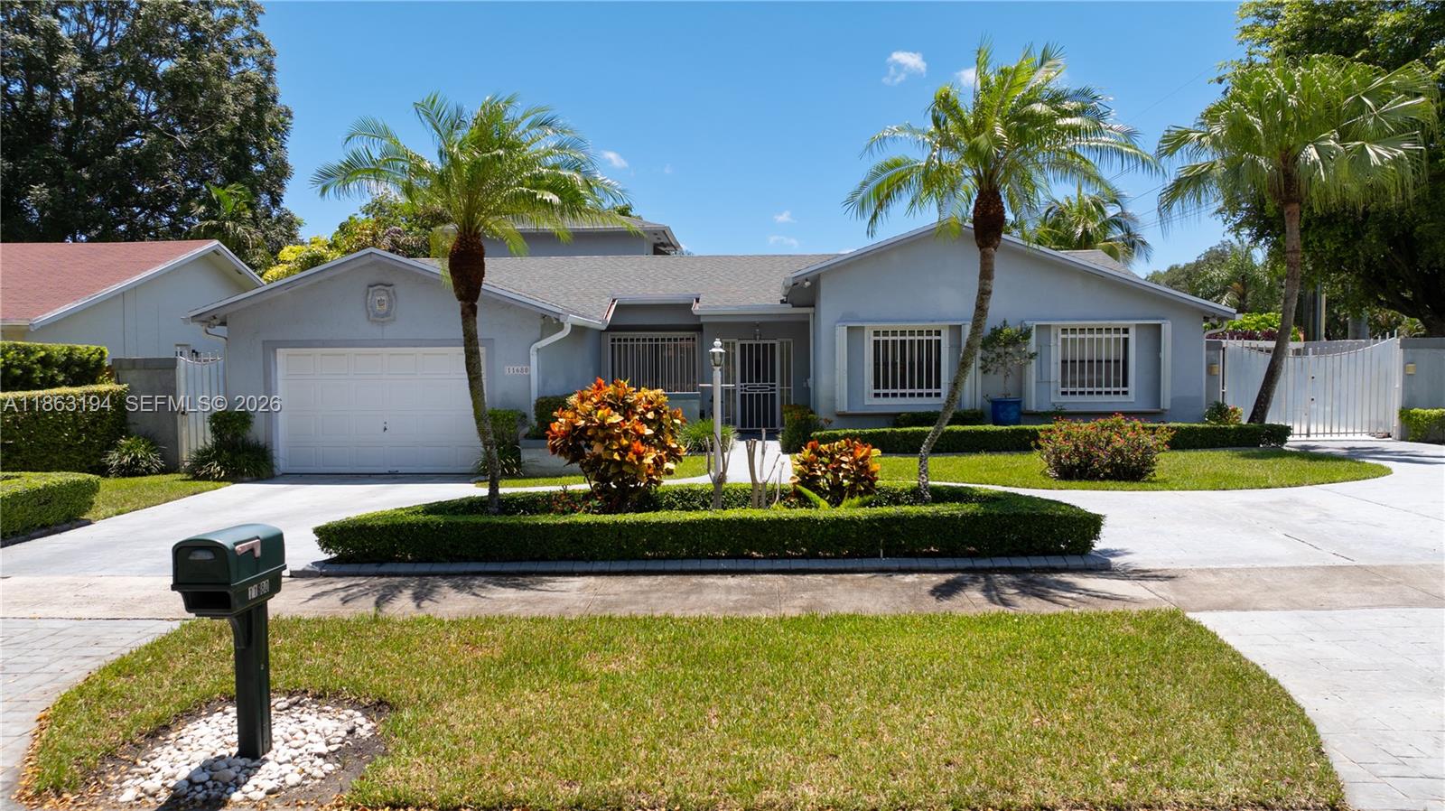 Light-blue single-story home with an attached garage, palm trees, and a gated driveway.