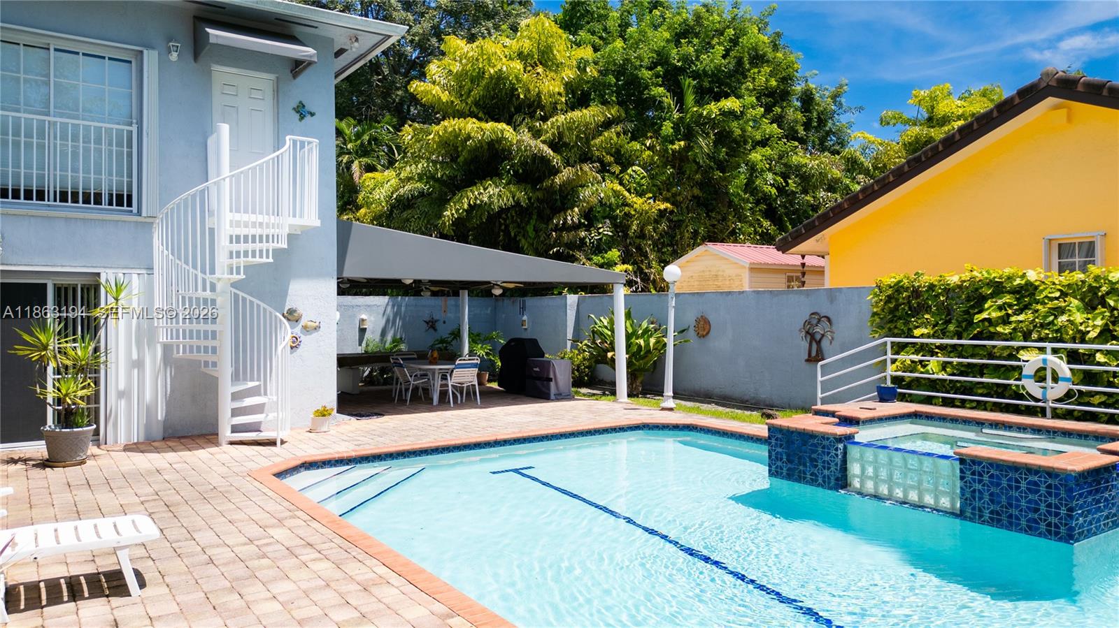 Backyard pool and raised spa beside a white spiral staircase and covered patio.