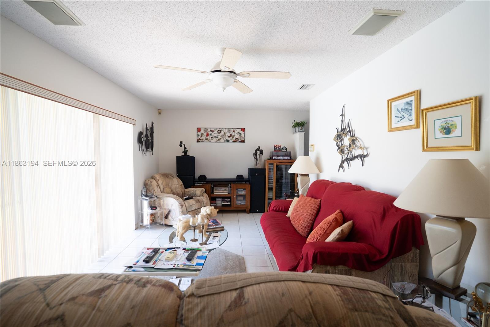 Living room with a red sofa, beige recliner, and vertical blinds over large sliding glass doors.
