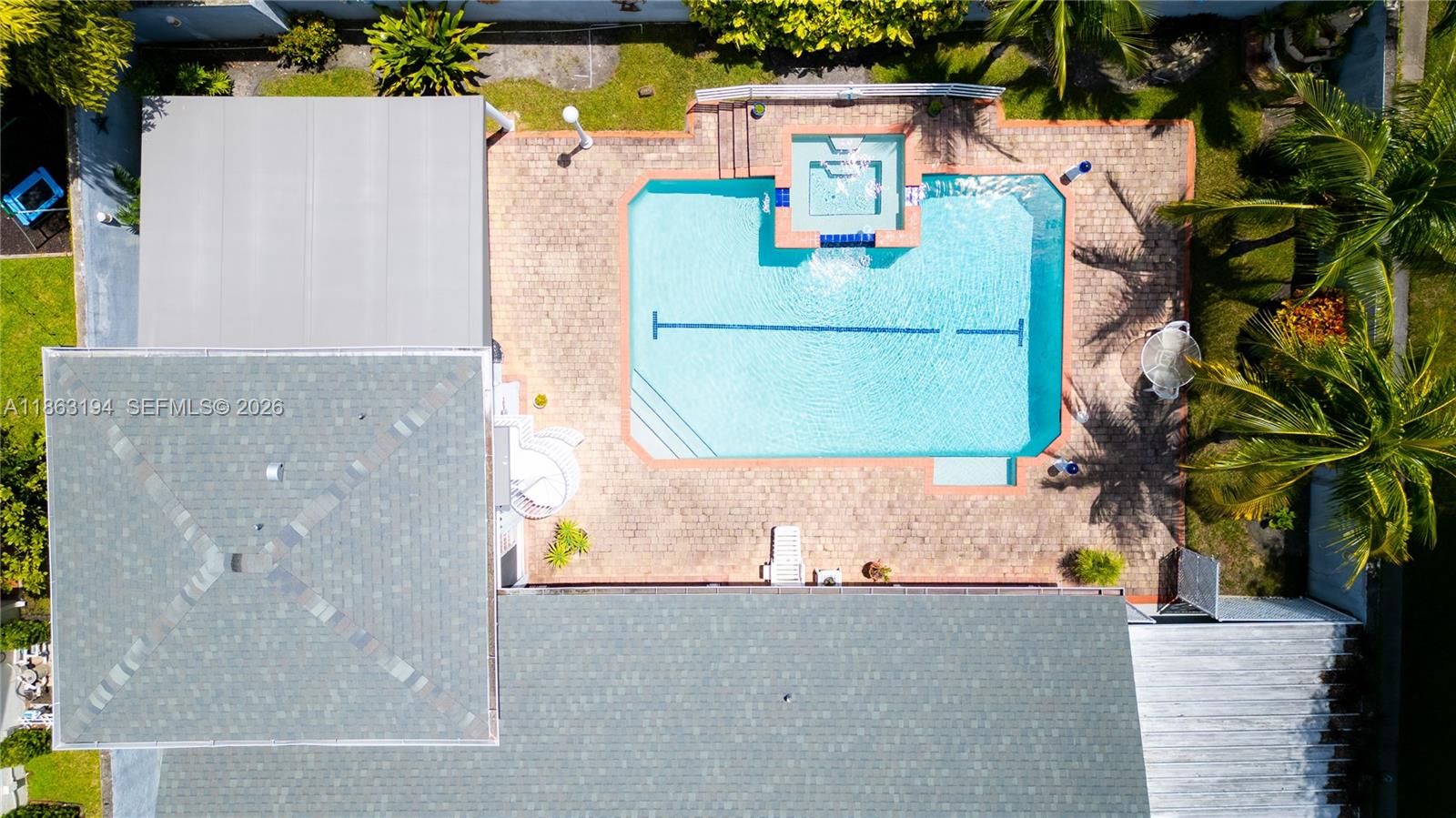 Aerial view of a backyard pool and raised spa surrounded by a paved patio and palm trees.