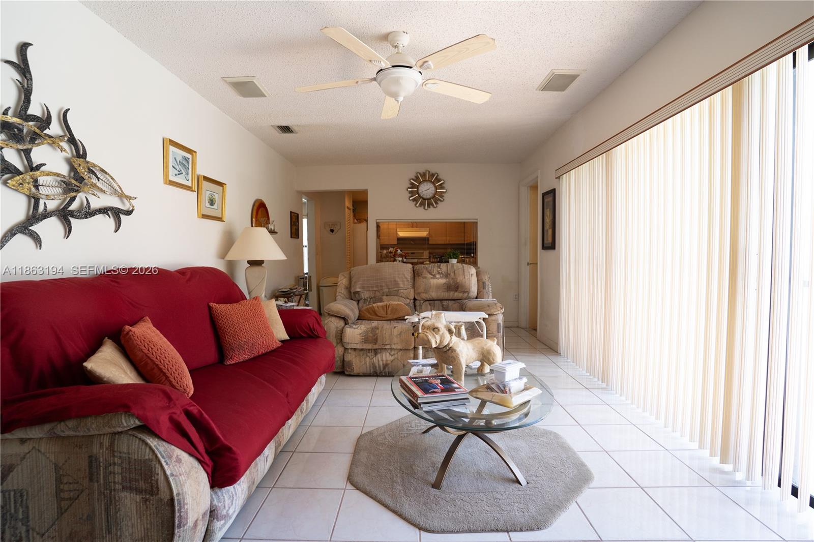 Living room with a red sofa, patterned recliners, and vertical blinds covering a large window.