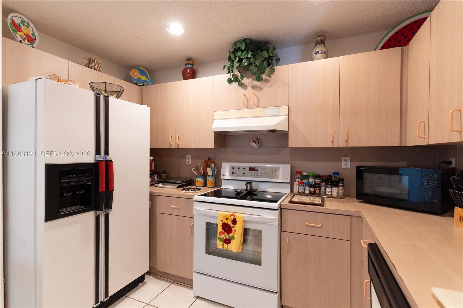 Kitchen with light wood cabinets, white appliances, and colorful decorative items above the cupboards.