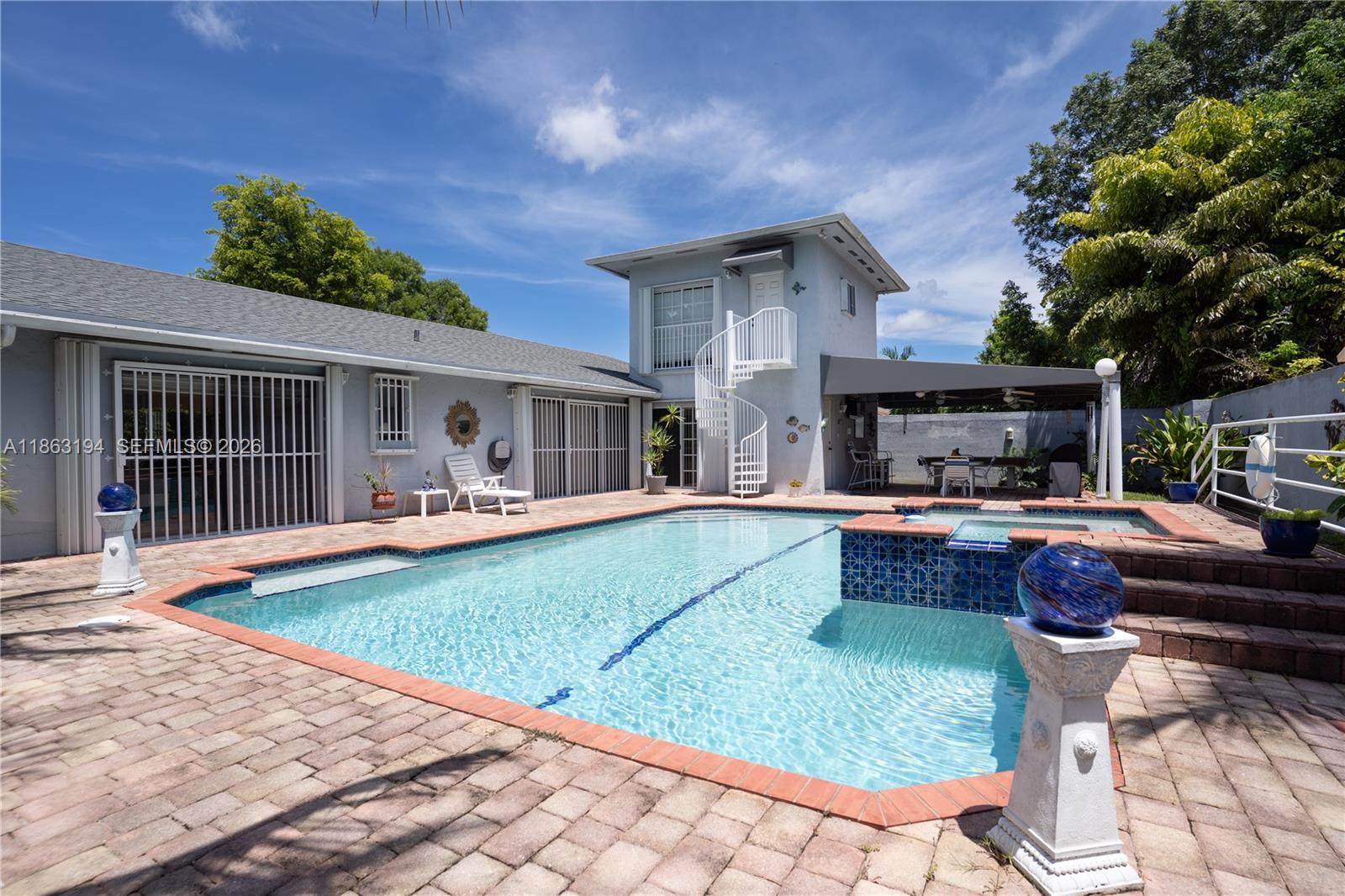 Backyard swimming pool beside a light-colored home with a spiral staircase and covered patio.