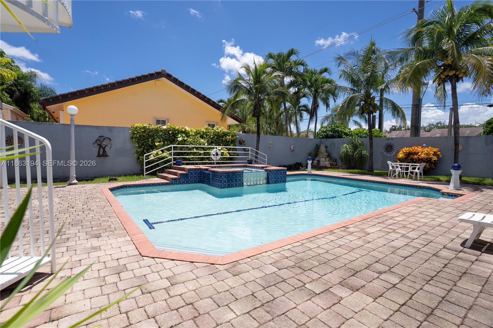 Backyard swimming pool with raised tiled spa, paver deck, and surrounding palm trees.