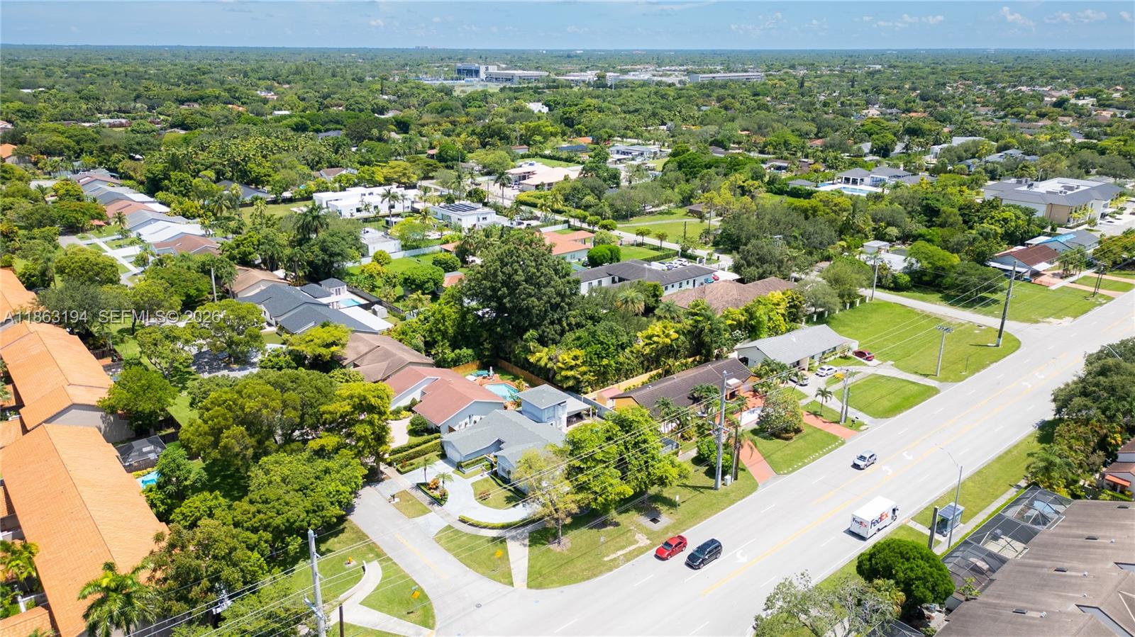 Aerial view of a leafy neighborhood with detached homes and a major road in the foreground.