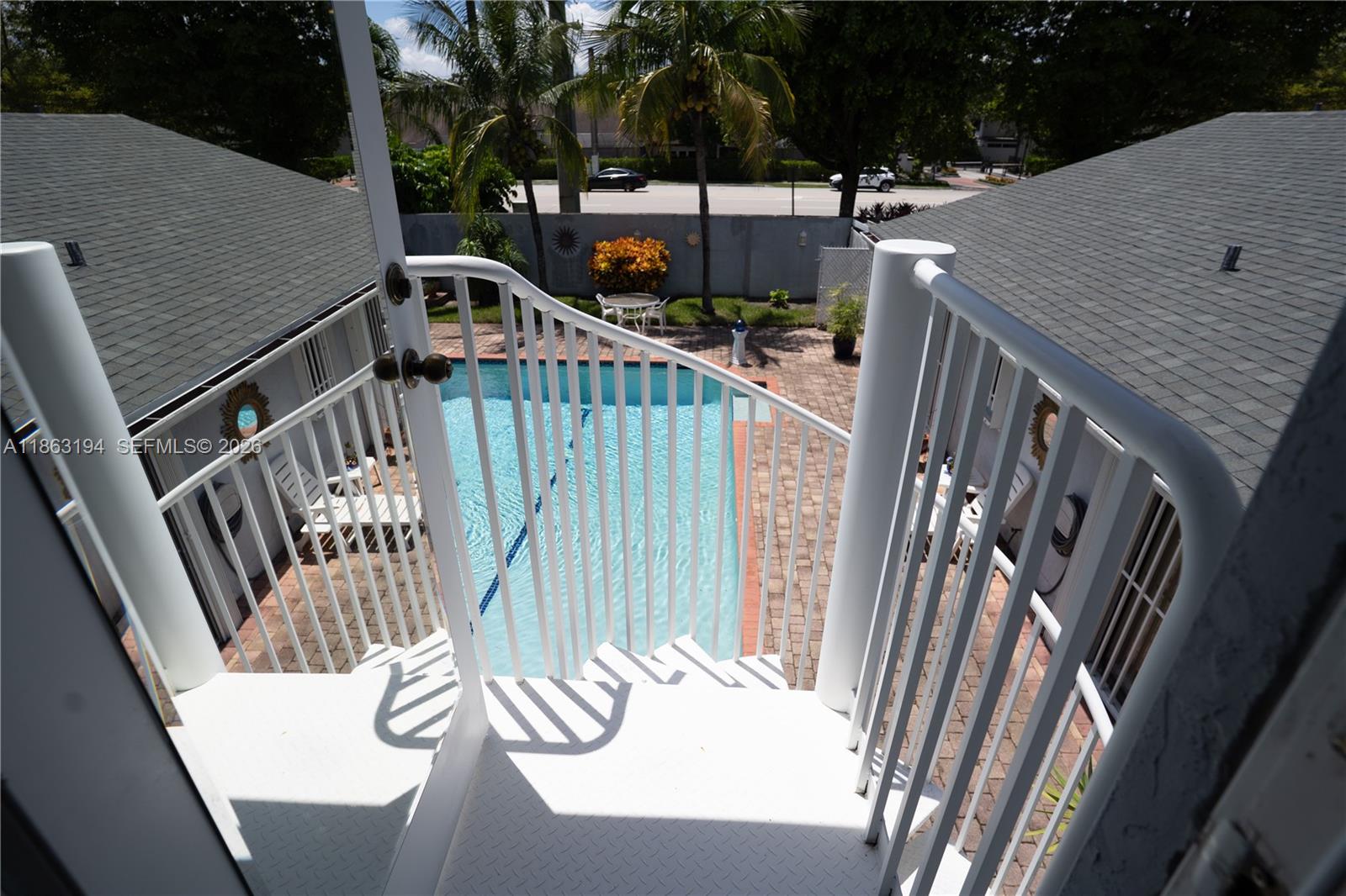 White-railed staircase overlooks a turquoise pool and brick-paved courtyard.