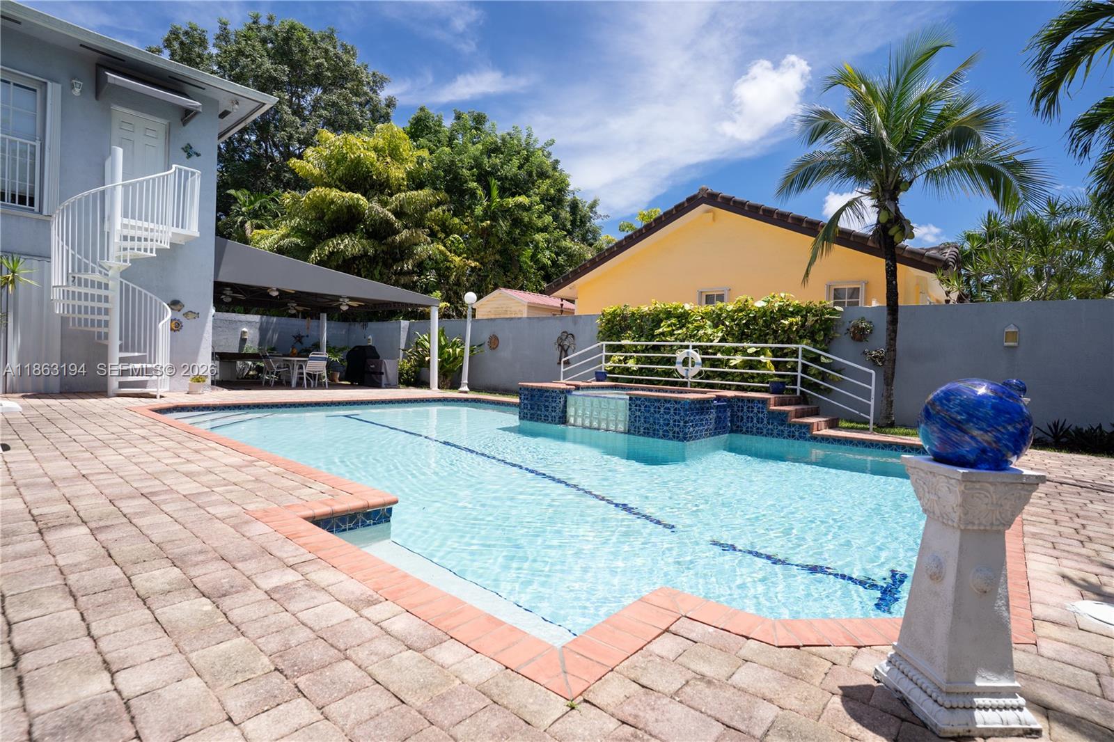 Backyard swimming pool with raised tiled spa, covered patio, and palm trees.