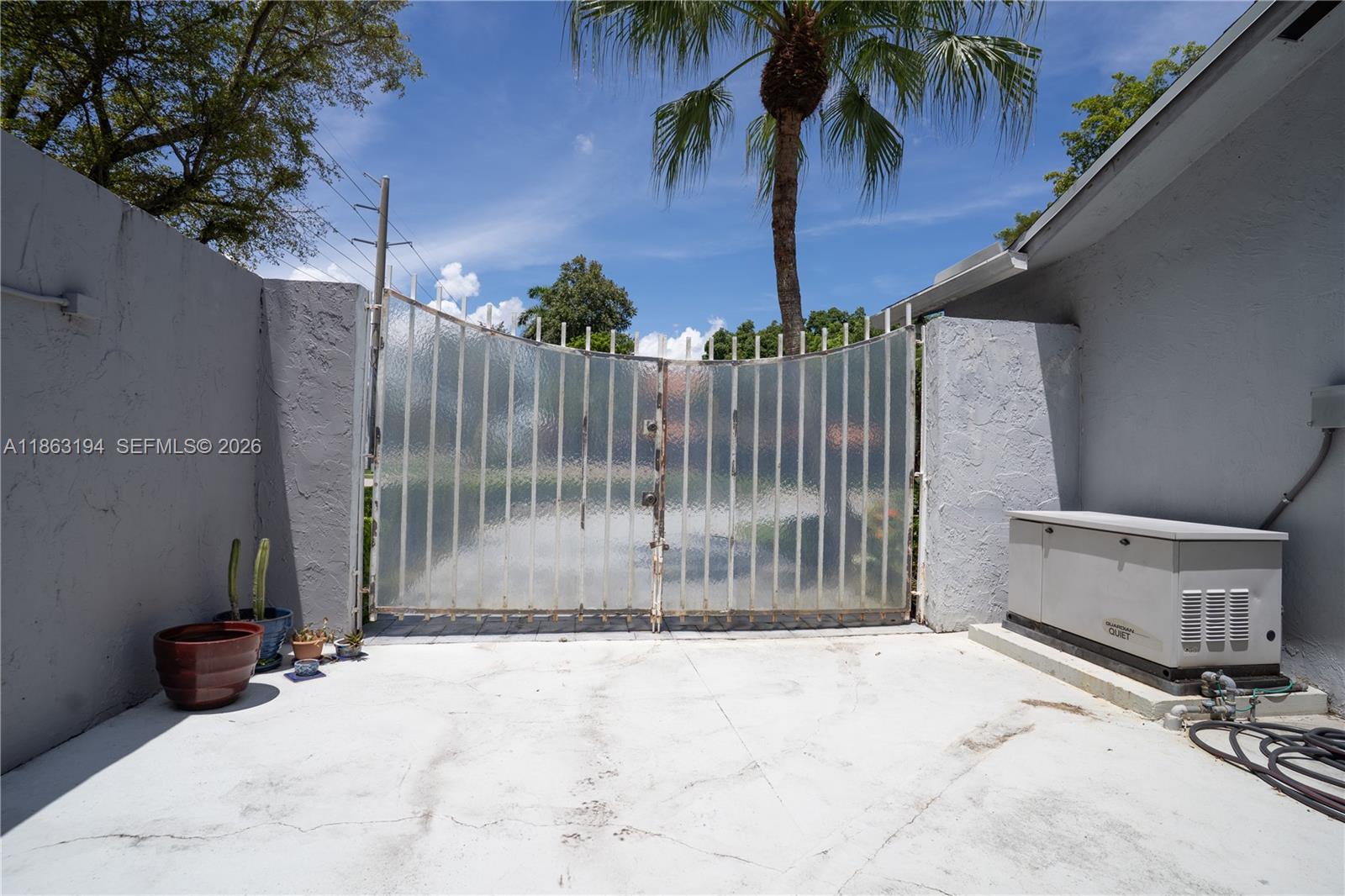 Paved side area with a tall frosted metal gate, gray stucco walls, and a standby generator.