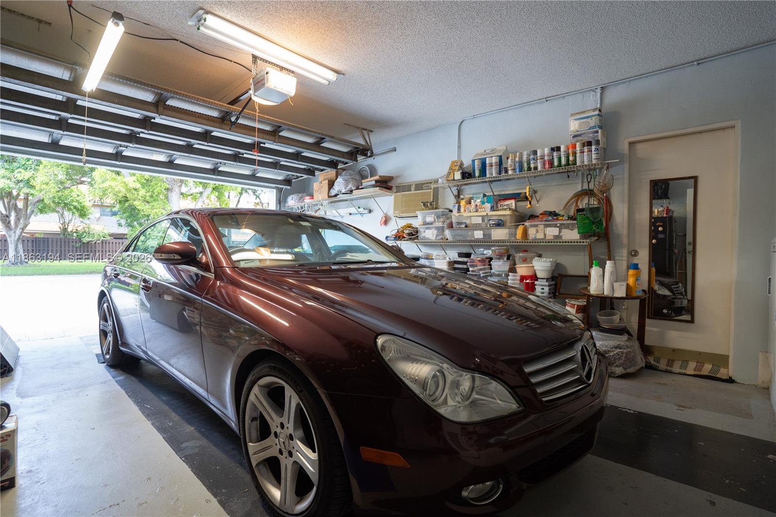 Garage with a maroon Mercedes beside storage shelves and an open overhead door.