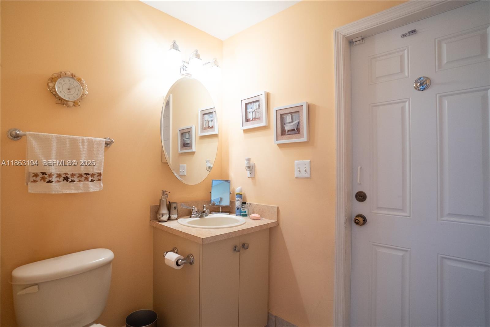 Bathroom with a beige vanity, oval mirror, toilet, and white paneled door.