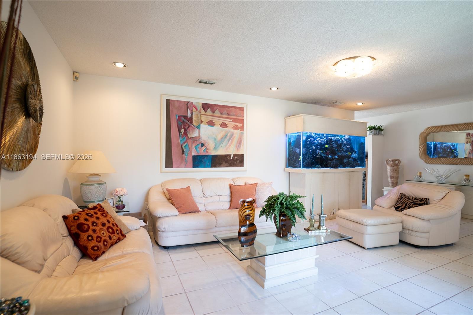 Living room with cream leather seating, a glass coffee table, and a large saltwater aquarium.