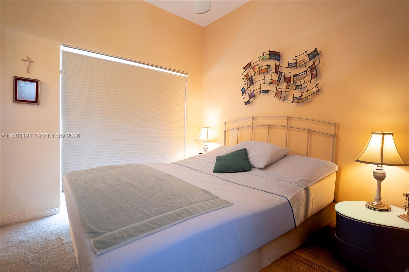 Bedroom with a metal headboard, green accent pillow, abstract wall art, and a large shaded window.