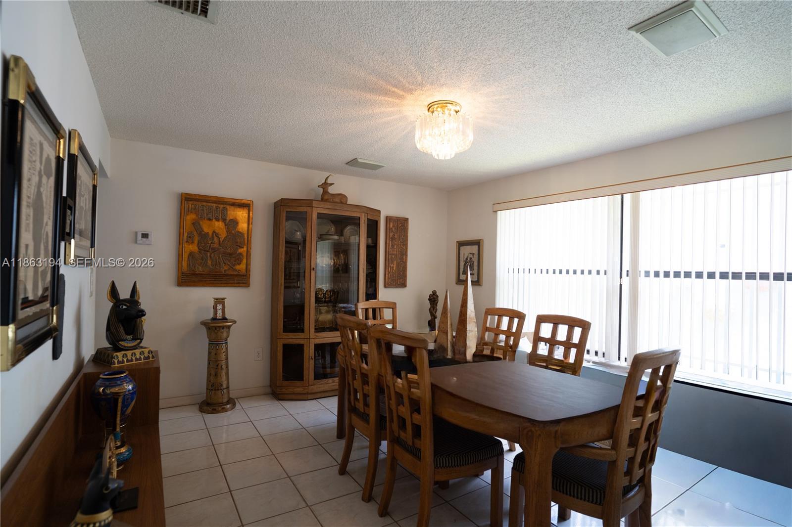 Dining room with a large wooden table, glass-front cabinet, and sliding doors with vertical blinds.