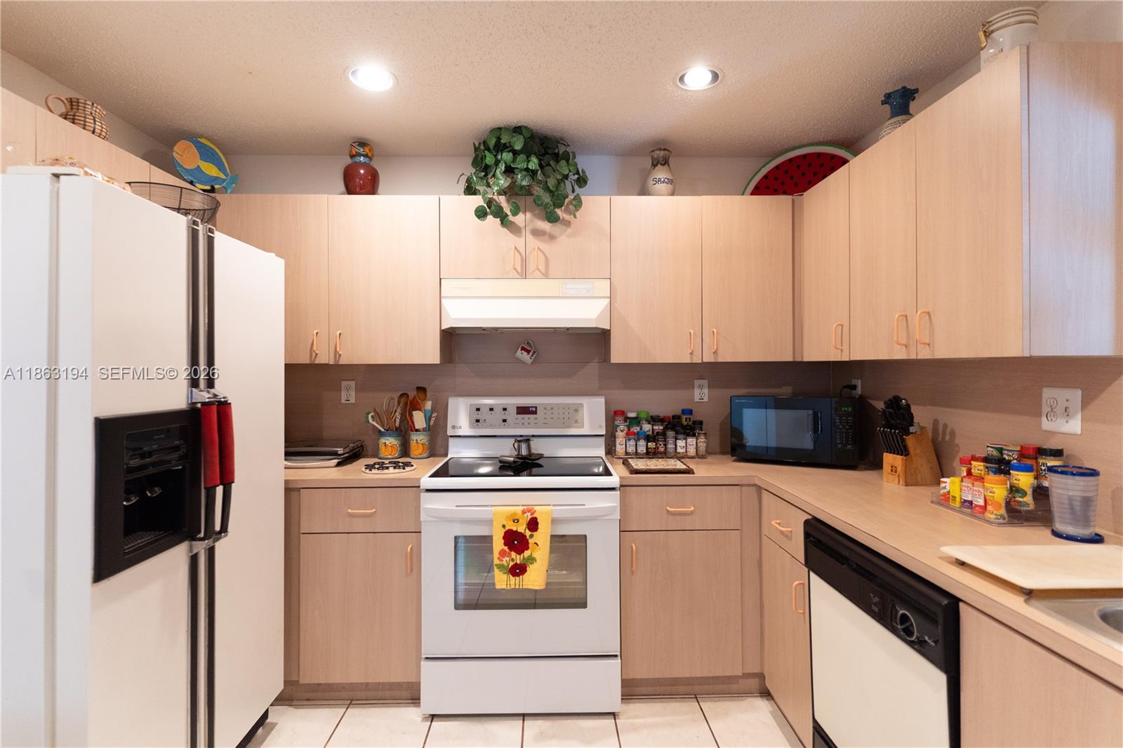 Kitchen with light wood cabinets, white appliances, and a tiled floor.