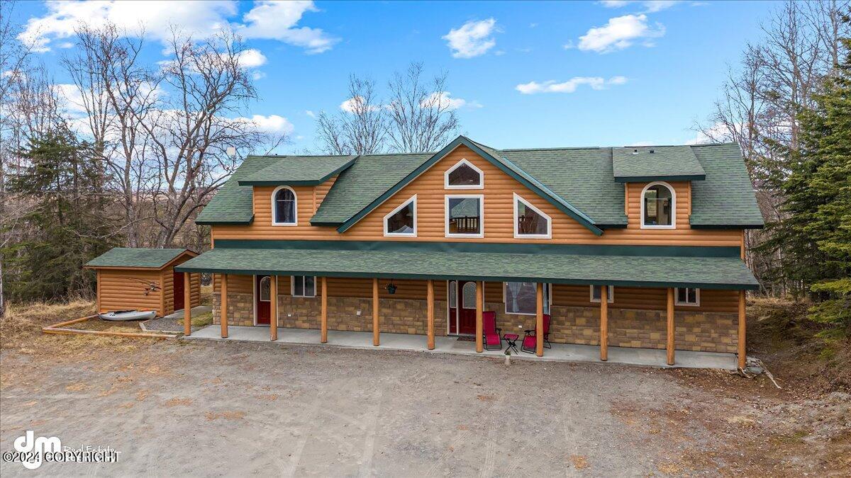 Log-sided house with a green roof and long covered porch, surrounded by trees.