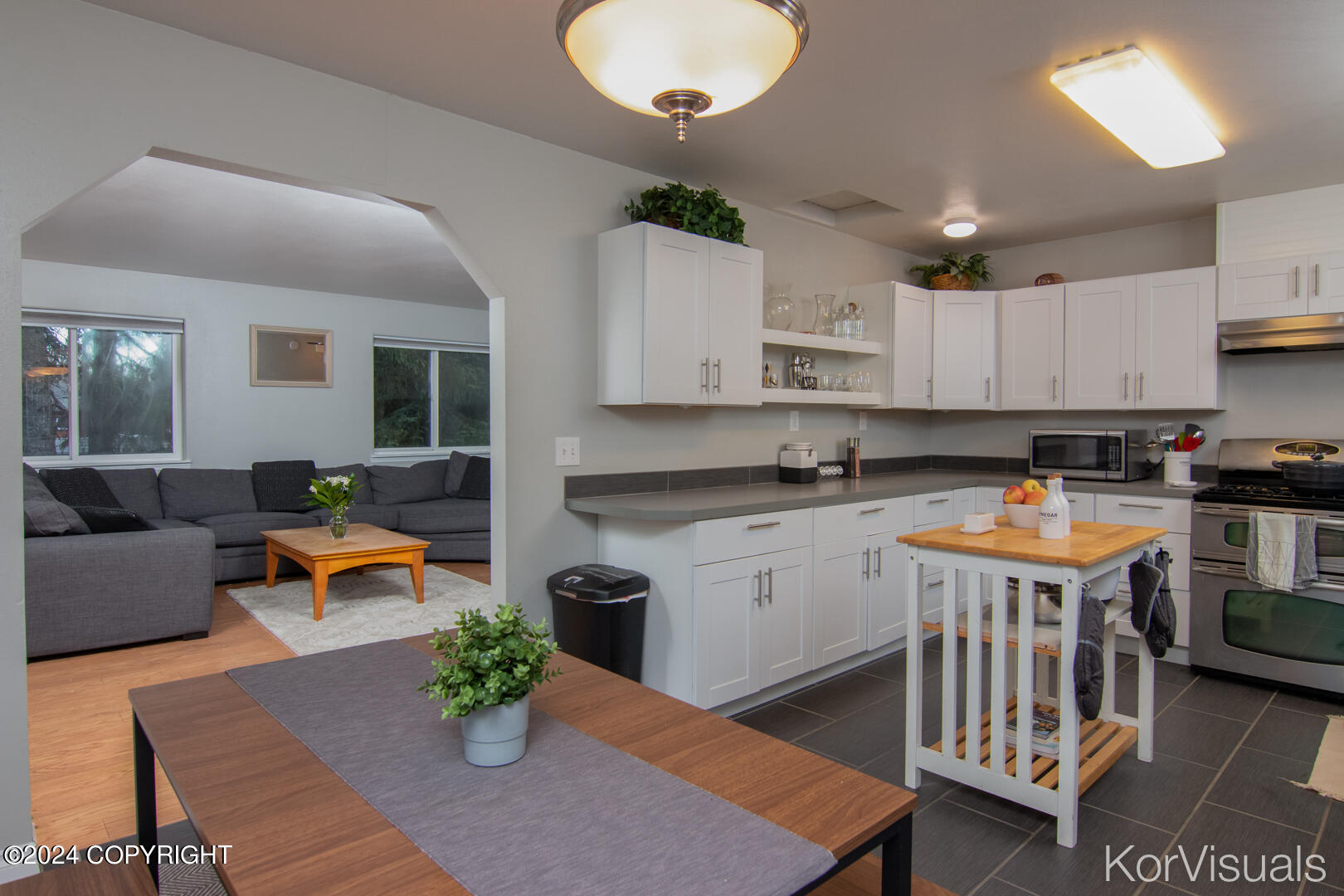 Kitchen with white cabinets and gray counters opening to a living room with a gray sectional.