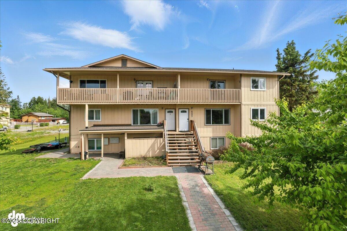 Beige multi-level home with a long balcony, exterior staircase, and brick walkway.