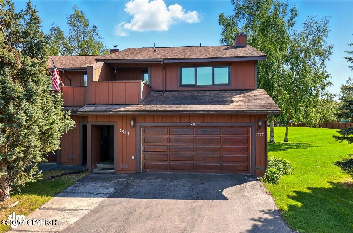 Two-story reddish-brown house with a double garage, upper balcony, and American flag.