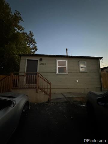 Green-sided home with a raised wooden porch, photographed at dusk from the driveway.